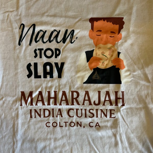 A white t-shirt with a cartoon man eating naan and the text "Naan Stop Slay Maharajah India Cuisine".