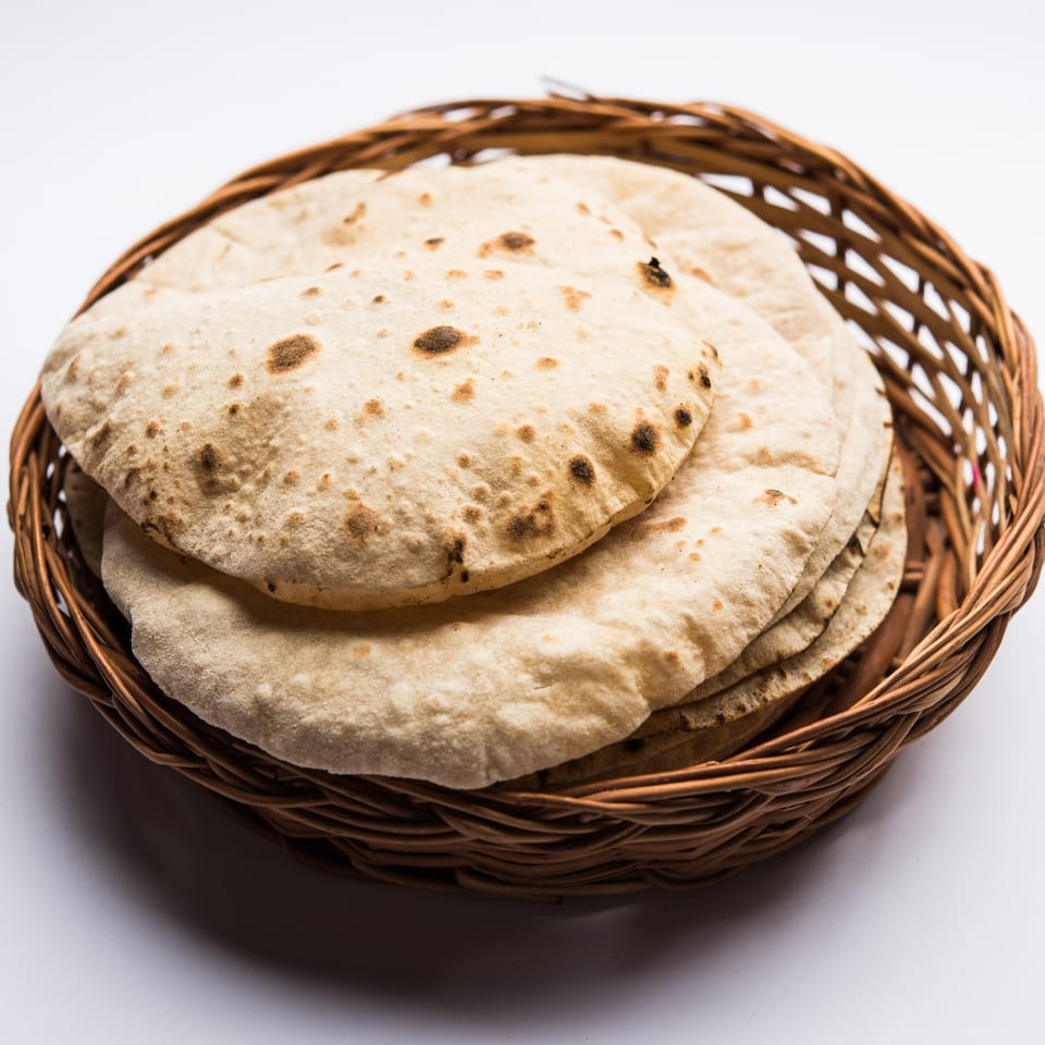 A woven basket filled with several round, flat Indian rotis, some with browned spots.