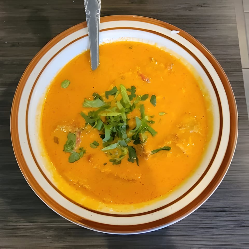 A bowl of vibrant orange Indian curry, garnished with fresh green cilantro, and a spoon.
