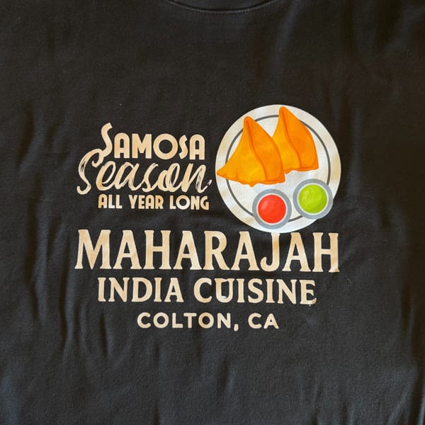 Black t-shirt with "Samosa Season All Year Long Maharajah India Cuisine Colton, CA" and samosa graphic.