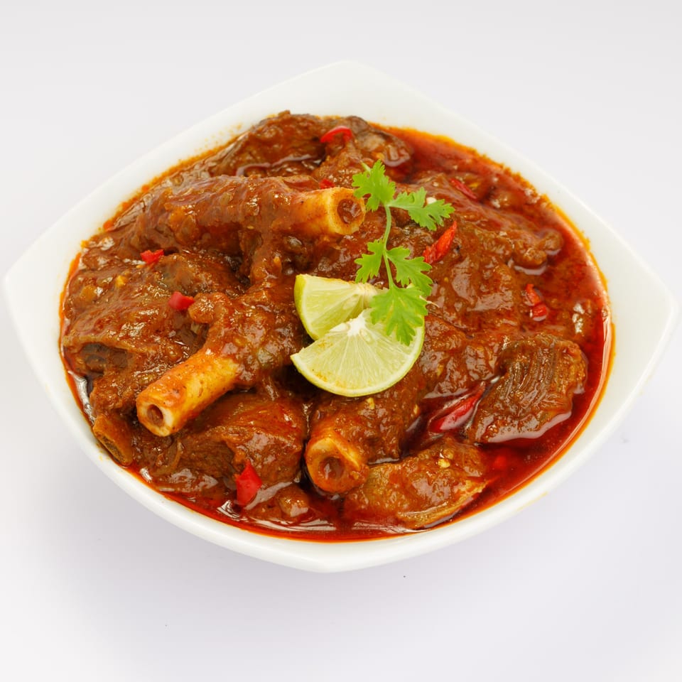 Maharajah India Cuisine's lamb curry, garnished with fresh cilantro and lime wedges in a white bowl.